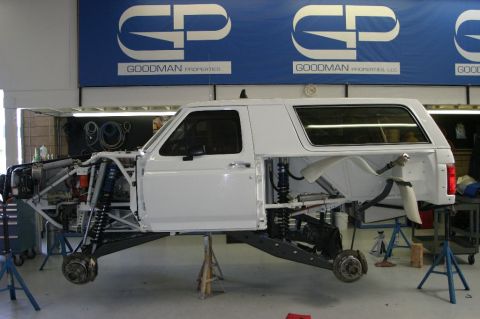 1996 Ford Bronco - A white Ford Bronco body shell mounted on a custom tubular prerunner chassis, shown in side profile up on jack stands in a shop. The build…