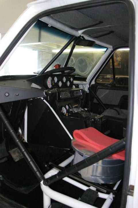 1996 Ford Bronco - Interior view of a stripped race/prerunner build showing a white welded roll cage, a custom black dash panel with a cluster of round analog…