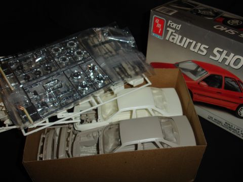 1993 Ford Taurus - The photo shows unassembled parts for a model car kit, including the chassis and body, along with a box for a Ford Taurus SHO model.