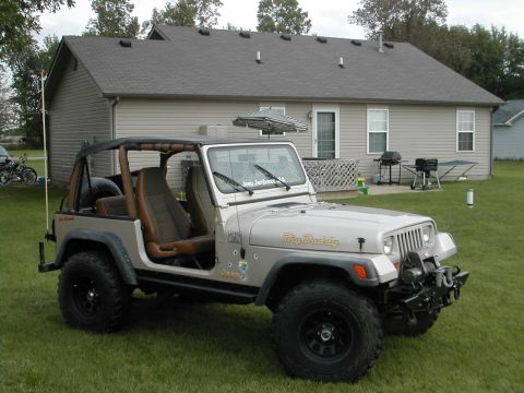 1998 Ford Crown Victoria - A silver Jeep Wrangler is parked on a grassy lawn in front of a suburban house.