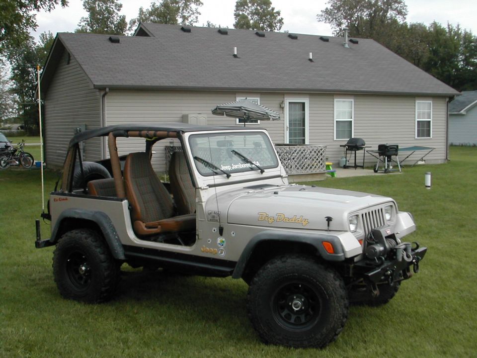 Silver Jeep Wrangler with "Big Daddy" on the hood, parked on grass in front of a house