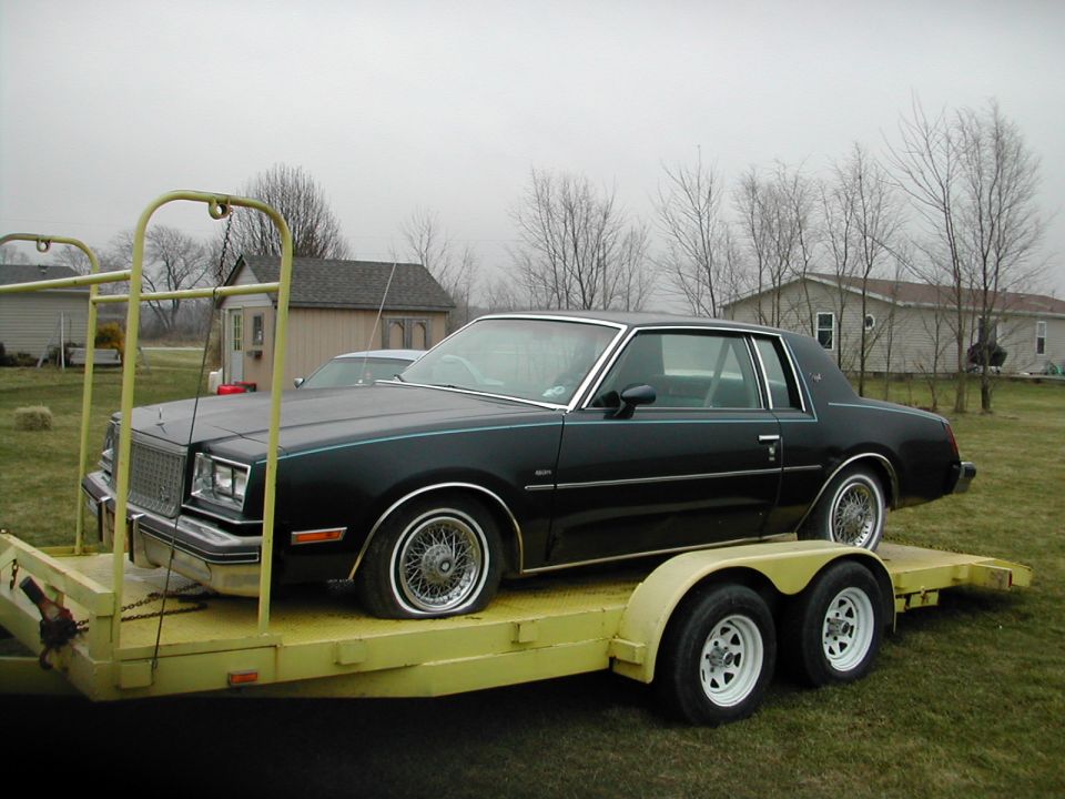 Black coupe with wire wheels on a yellow trailer