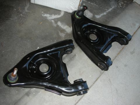 1998 Ford Crown Victoria - Two freshly black-painted front lower control arms with ball joints laid on a concrete garage floor.