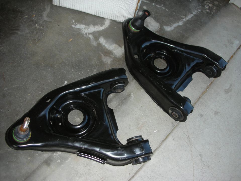 Pair of black-painted front lower control arms on concrete floor