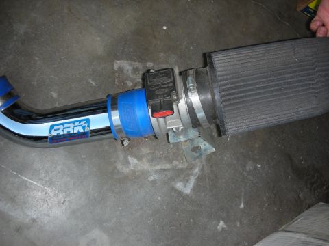 1998 Ford Crown Victoria - close-up of a chrome BBK intake pipe joined by a blue coupler to a mass-air sensor and cone filter on concrete.