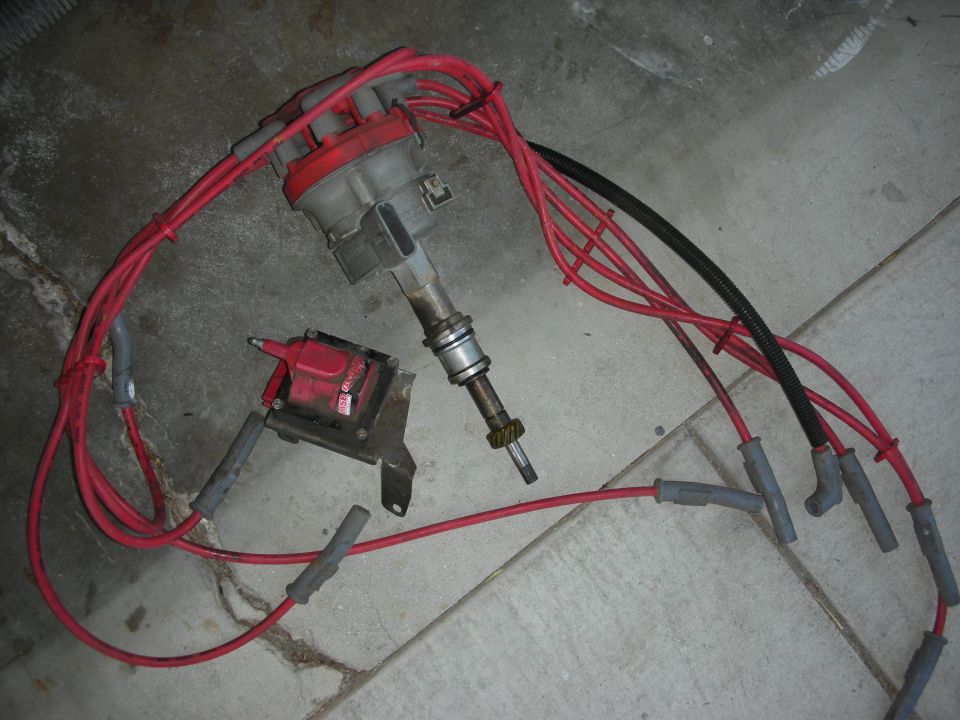 Distributor, ignition coil, and red spark plug wires laid out on a concrete floor