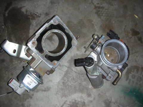 1998 Ford Crown Victoria - Two throttle body parts are shown on a concrete surface.