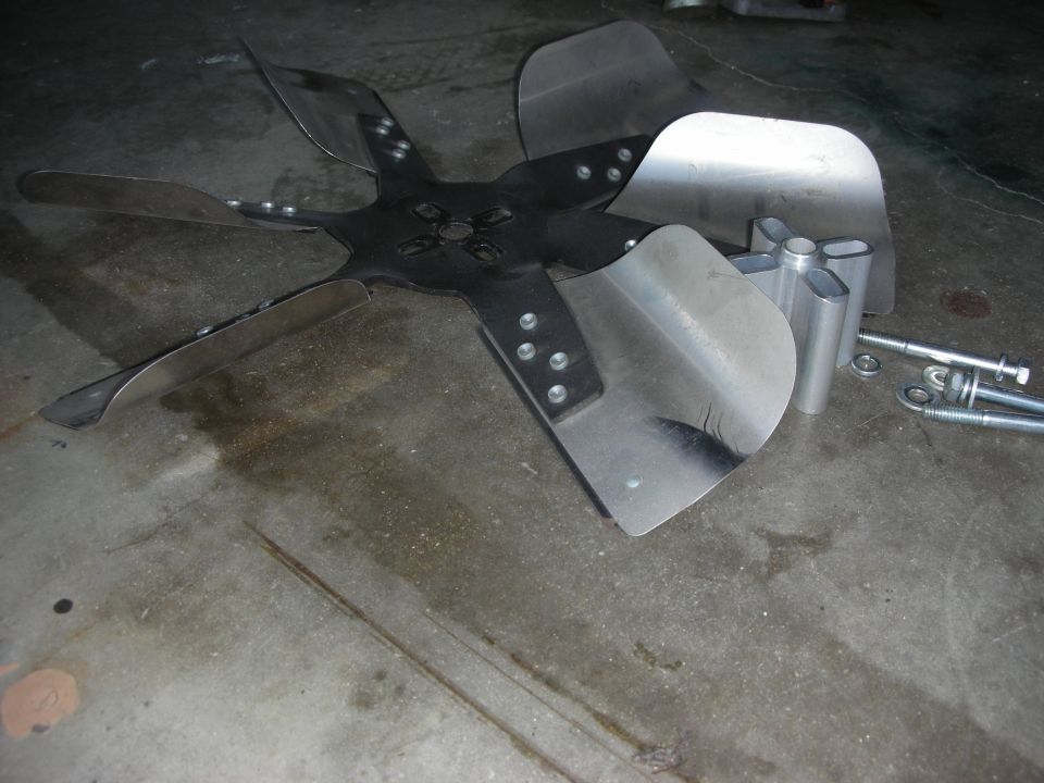 Metal radiator fan blade with six blades, next to aluminum spacers and bolts on a concrete floor