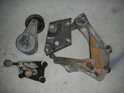 1998 Ford Crown Victoria - Several engine belt tensioner and bracket components are laid out on a gray surface.