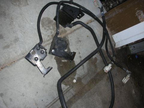 1998 Ford Crown Victoria - A collection of automotive parts, including a wiring harness and latches, lies on a concrete surface.