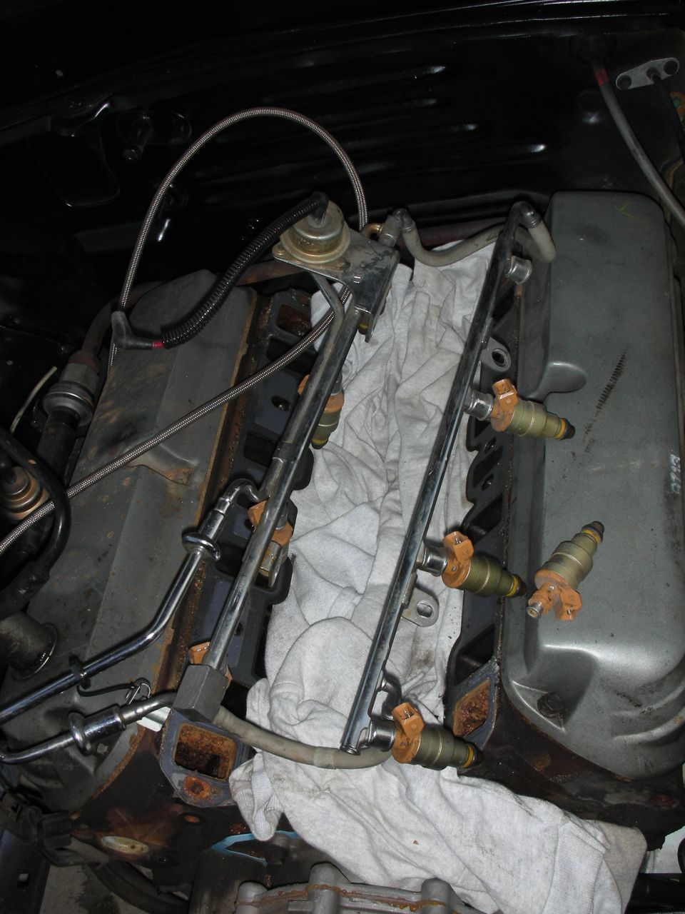 Engine fuel rail with injectors removed, resting on a cloth over engine components
