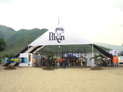 1995 Ford F-150 - An outdoor event is underway under a large tent with a prominent beer logo, set against a backdrop of rolling hills.