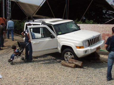 1995 Ford F-150 - White Jeep Commander SUV with front passenger door open, parked on gravel with logs under front tire.