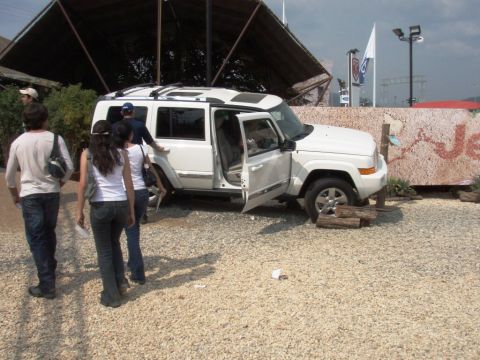 1995 Ford F-150 - White Jeep Commander with doors open, front passenger side propped on logs, with people walking nearby.