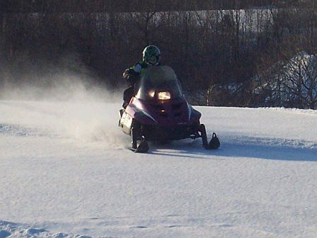 Rider on purple snowmobile spraying snow across a snowy field