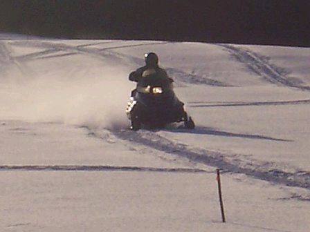 1996 Arctic Cat Puma - A snowmobile is ridden across a snow-covered landscape, leaving tracks behind.