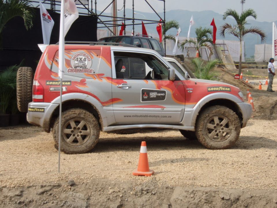 Silver and red Mitsubishi Montero 4x4 with racing decals and a spare tire on the back, parked on a dirt track
