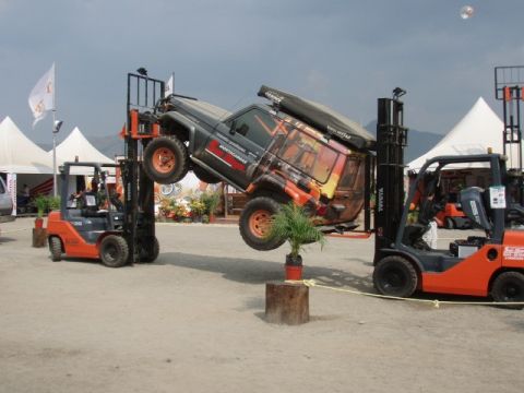 1995 Ford F-150 - Two forklifts lift a Toyota Land Cruiser, displaying its off-road capabilities and rooftop tent setup.