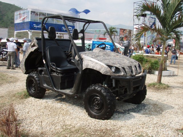 Camouflaged utility vehicle with black seats and roll cage, parked on gravel
