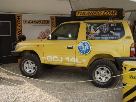 1995 Ford F-150 - Yellow Toyota Land Cruiser Prado modified for off-road use, a roof tent and sponsor decals.