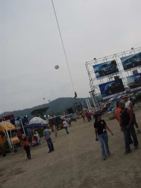 1995 Ford F-150 - An outdoor event features large billboards displaying vehicles, with a person suspended on a wire overhead.