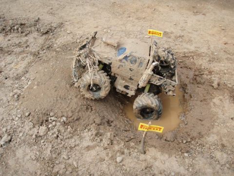 1995 Ford F-150 - Overhead view of a mud-caked radio-control rock crawler or trail truck sitting in a small water-filled rut on a dirt course, with yellow Pi…