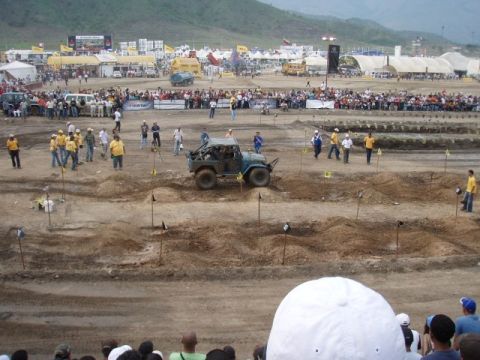 1995 Ford F-150 - An off-road vehicle navigates a dirt course during an event with crowds and vendor tents.