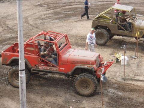 1995 Ford F-150 - A red Jeep Rubicon, modified with a roll cage, sits in a dirt lot with another vehicle in the background.