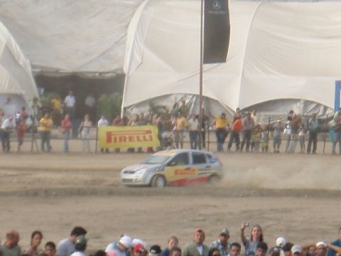 1995 Ford F-150 - A rally car races on a dirt track, with a crowd watching behind a Pirelli banner.