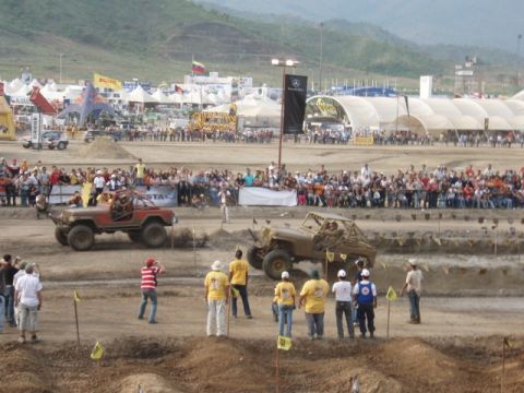 1995 Ford F-150 - Off-road vehicles race in front of a large crowd at an event with tents and banners.