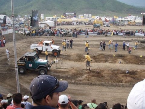 1995 Ford F-150 - Off-road vehicles compete in a dirt arena with spectators watching from the stands.