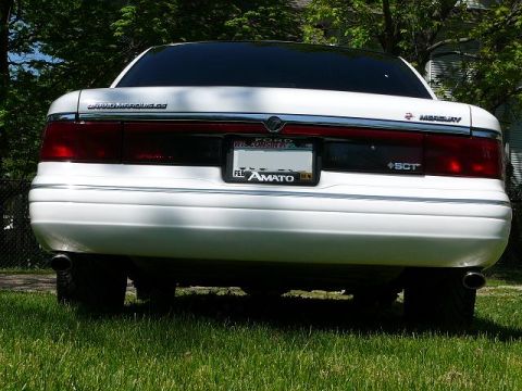 1997 Mercury Grand Marquis - Low rear view of a white Mercury Grand Marquis LS on grass, showing the full-width red taillight panel with the Mercury emblem, "GRAND MARQ…
