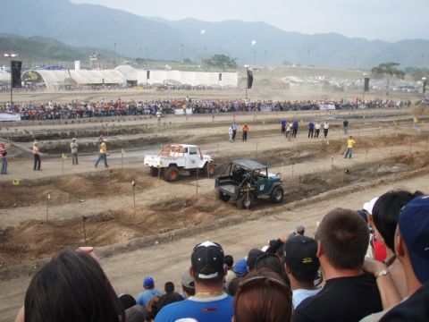 1995 Ford F-150 - Two off-road vehicles compete on a dirt track during an event with a large crowd watching.