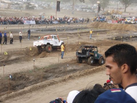 1995 Ford F-150 - Two off-road vehicles compete on a dirt track during an event with a crowd watching.