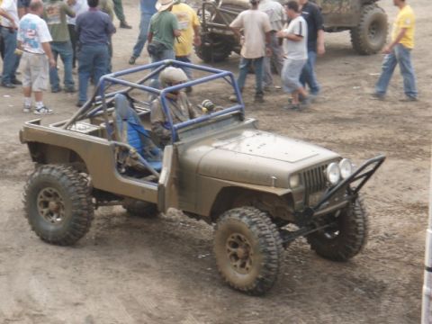 1995 Ford F-150 - A modified Jeep with a roll cage and off-road tires sits in a muddy area with spectators around.