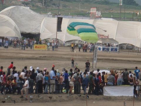 1995 Ford F-150 - Spectators gather to watch a parachute descent at an outdoor event with large tents and sponsor banners visible.