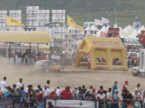 1995 Ford F-150 - A rally car races on a dirt track in front of a crowd, with inflatable structures and flags visible in the background.