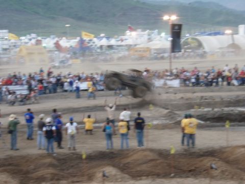 1995 Ford F-150 - A monster truck is captured mid-air during a jump at an outdoor event with spectators in the background.