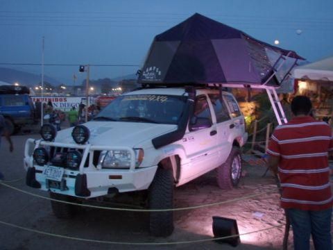 1995 Ford F-150 - A white Jeep Grand Cherokee is outfitted with a rooftop tent and off-road accessories, parked outdoors at dusk.