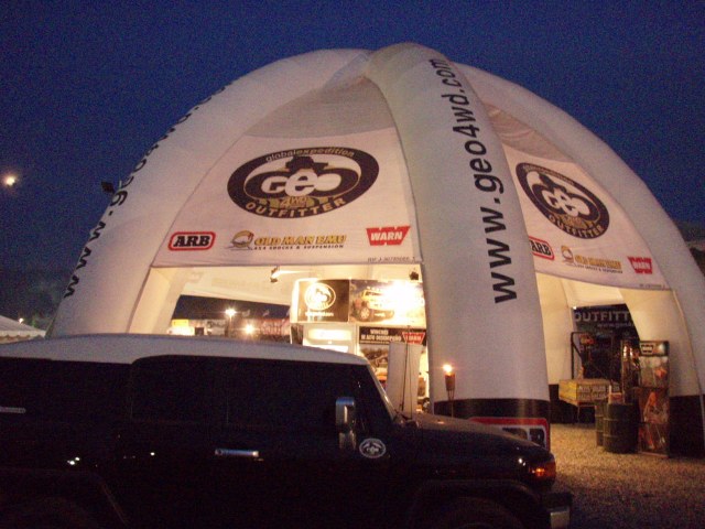 Dark SUV parked in front of a large white inflatable tent with 'GEO OUTFITTER' and 'www.geo4wd.com' logos. Supermotors.net logo at bottom right