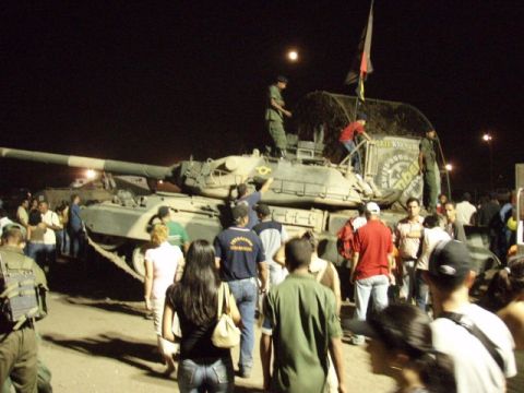 1995 Ford F-150 - A tank is surrounded by a crowd of people at night, with some individuals on top of the vehicle.