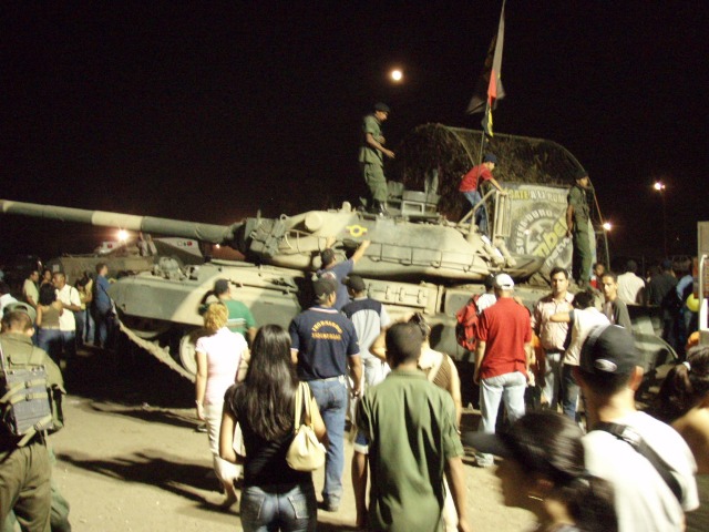 Tank with a crowd of people gathered around it at night