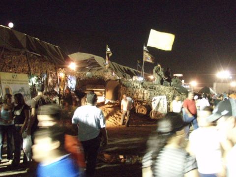 1995 Ford F-150 - A camouflaged military vehicle is displayed at an outdoor event at night, with a crowd of people gathered around.
