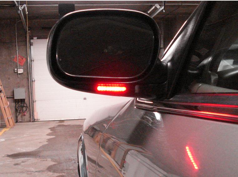 Side mirror with LED turn signal strip illuminated, reflecting on the car's fender