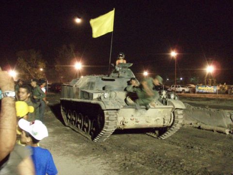 1995 Ford F-150 - Night shot of a tracked armored military vehicle running through a muddy field course, with a yellow flag on a mast and crew in camouflage…
