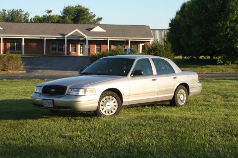 2004 Ford Crown Victoria - A silver 2004 Ford Crown Victoria is parked on a grassy lawn in front of a commercial building.