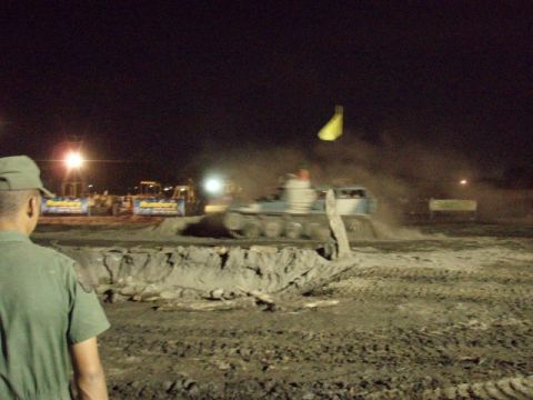 1995 Ford F-150 - A monster truck churns up mud during an event at night, with other vehicles visible in the distance.