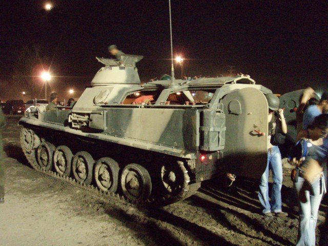 Tracked armored vehicle with a turret, people standing around it at night