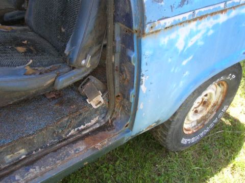 1992 Ford Mustang - The interior of a weathered blue vehicle reveals worn seats, a seatbelt, and visible rust on the door frame.