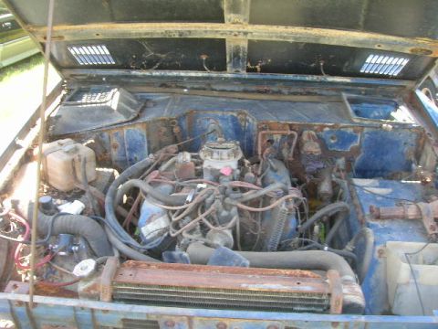 1992 Ford Mustang - The engine compartment of a weathered blue SUV is visible with the hood open, revealing its mechanical components.